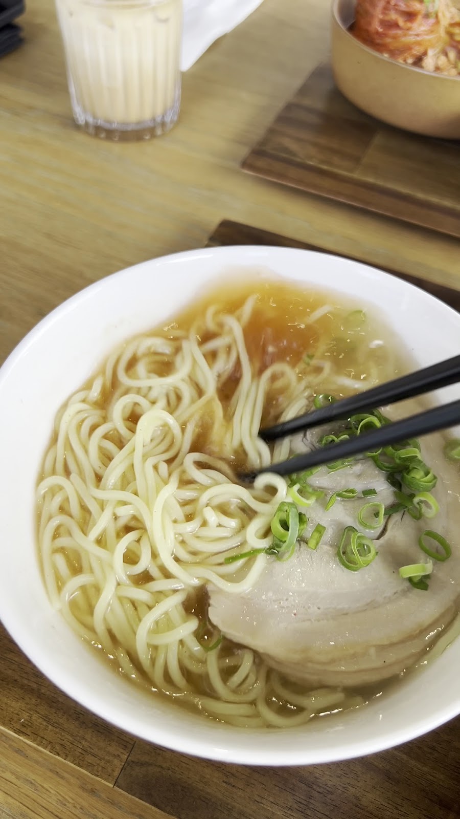 A bowl of noodle soup with sliced pork and spring onion at Minari, kimchi on the side