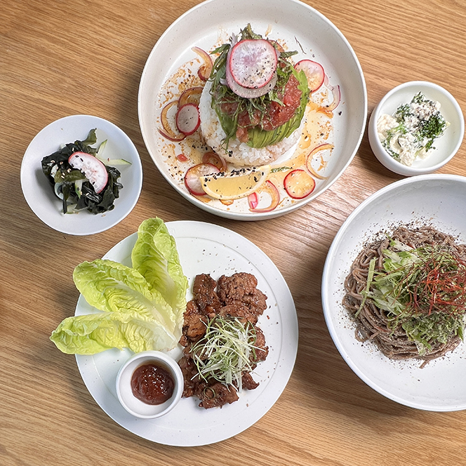 A spread of Minari dishes from above: a tuna and avocado rice bowl, marinated meat with lettuce, buckwheat noodle salad and side dishes